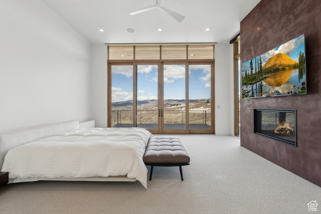 Carpeted bedroom featuring expansive windows, access to exterior, a glass covered fireplace, and recessed lighting