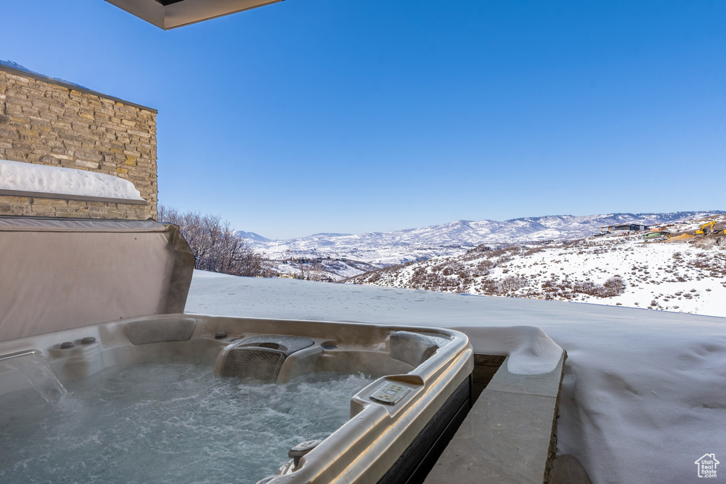 Snow covered patio featuring a hot tub and a mountain view