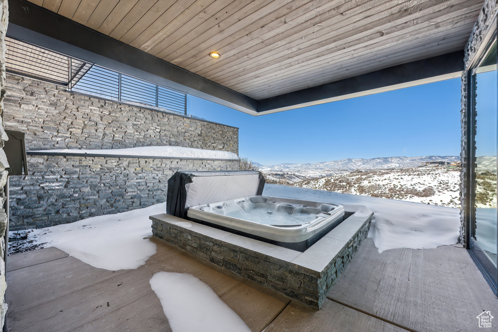 Snow covered patio with a mountain view and a covered hot tub
