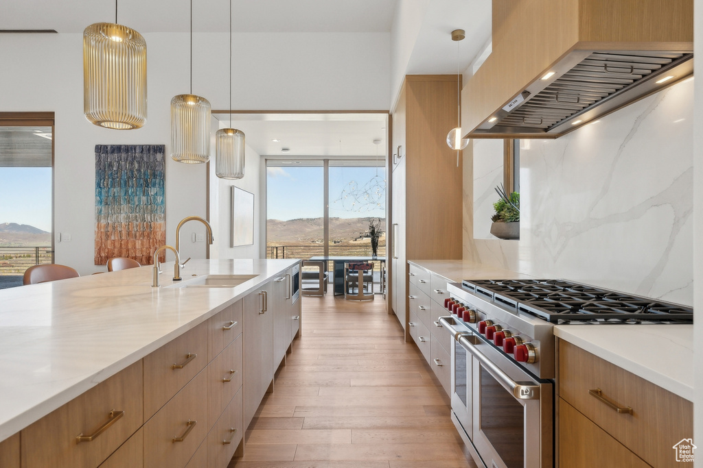 Kitchen with high end stove, a sink, wall chimney range hood, light wood-style floors, and a mountain view