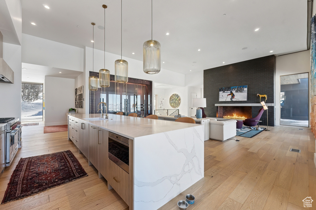Kitchen with light stone counters, hanging light fixtures, light hardwood / wood-style flooring, and a large island with sink