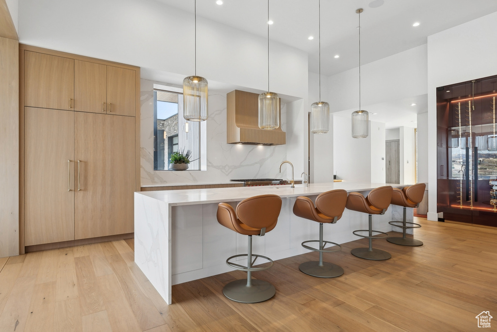 Kitchen with light wood-style flooring, modern cabinets, ventilation hood, a kitchen bar, and light countertops