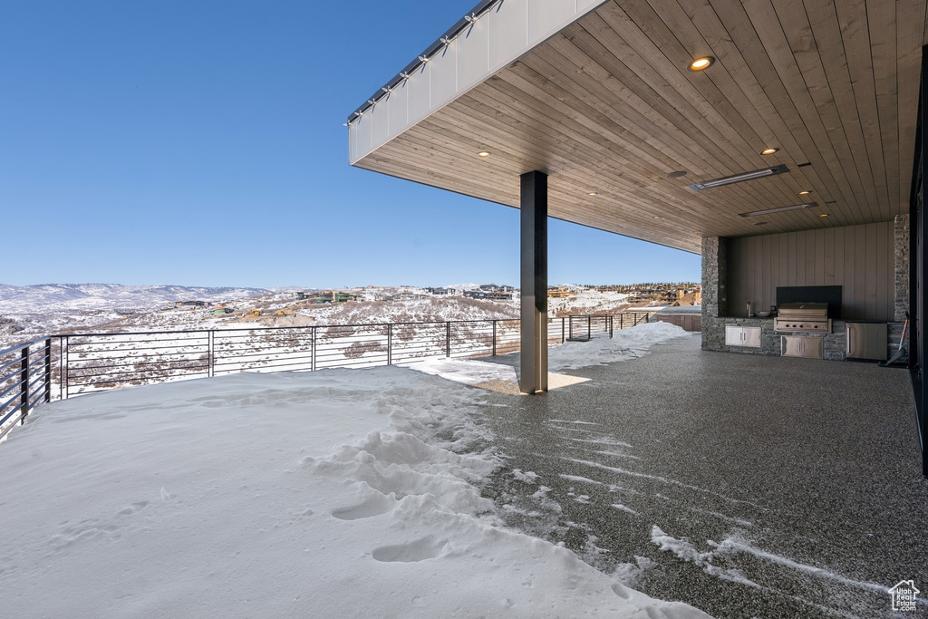 Snow covered patio featuring a mountain view, a grill, and an outdoor kitchen