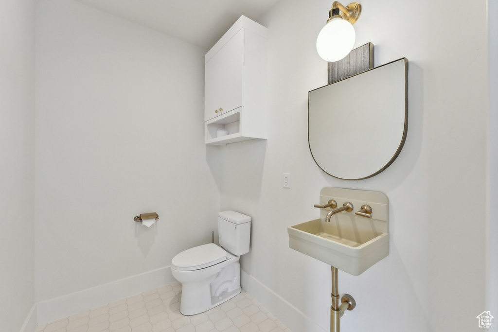 Half bath featuring baseboards, toilet, a sink, and tile patterned flooring