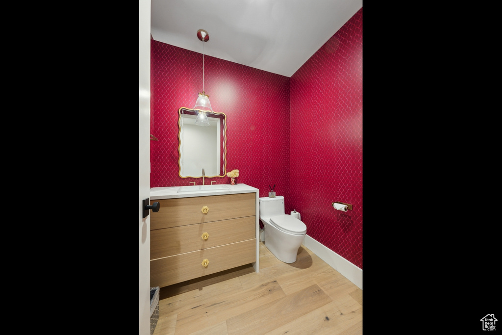 Half bathroom with wallpapered walls, toilet, wood finished floors, vanity, and baseboards