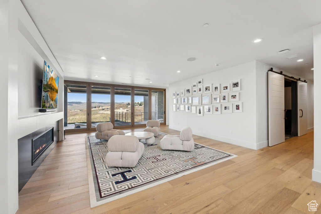 Living area with a barn door, a glass covered fireplace, light wood-type flooring, recessed lighting, and baseboards