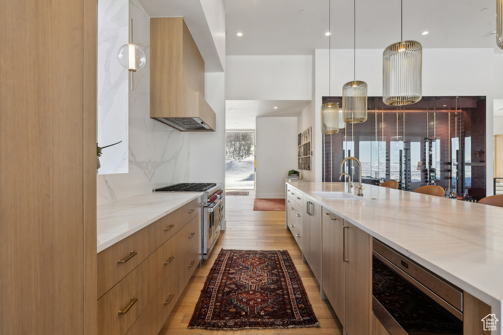 Kitchen featuring pendant lighting, sink, stainless steel stove, light stone counters, and custom exhaust hood