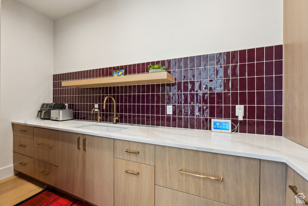 Kitchen with light stone countertops, sink, dark wood-type flooring, and decorative backsplash