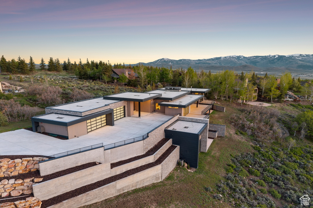Back of property at dusk with driveway, a mountain view, an outbuilding, and an exterior structure