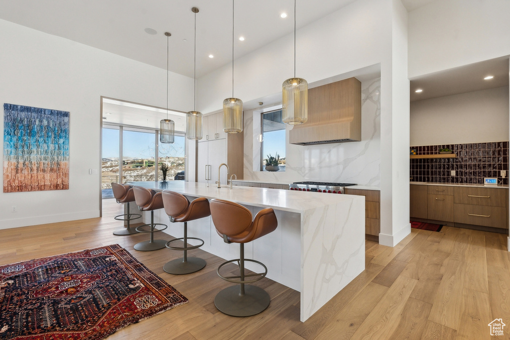 Kitchen with decorative light fixtures, light wood-type flooring, a kitchen breakfast bar, a large island, and decorative backsplash