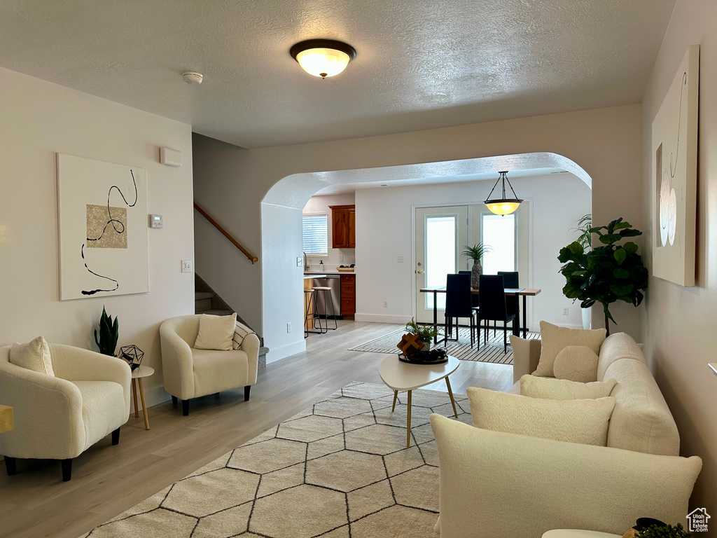 Living area with light wood-type flooring, baseboards, stairway, a textured ceiling, and arched walkways