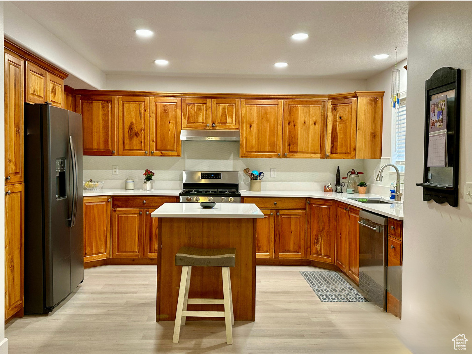 Kitchen featuring a kitchen island, appliances with stainless steel finishes, sink, a kitchen bar, and light wood-type flooring