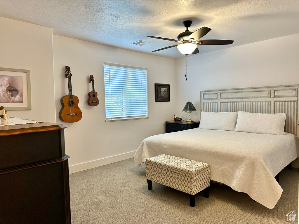 Bedroom with light carpet, ceiling fan, and a textured ceiling