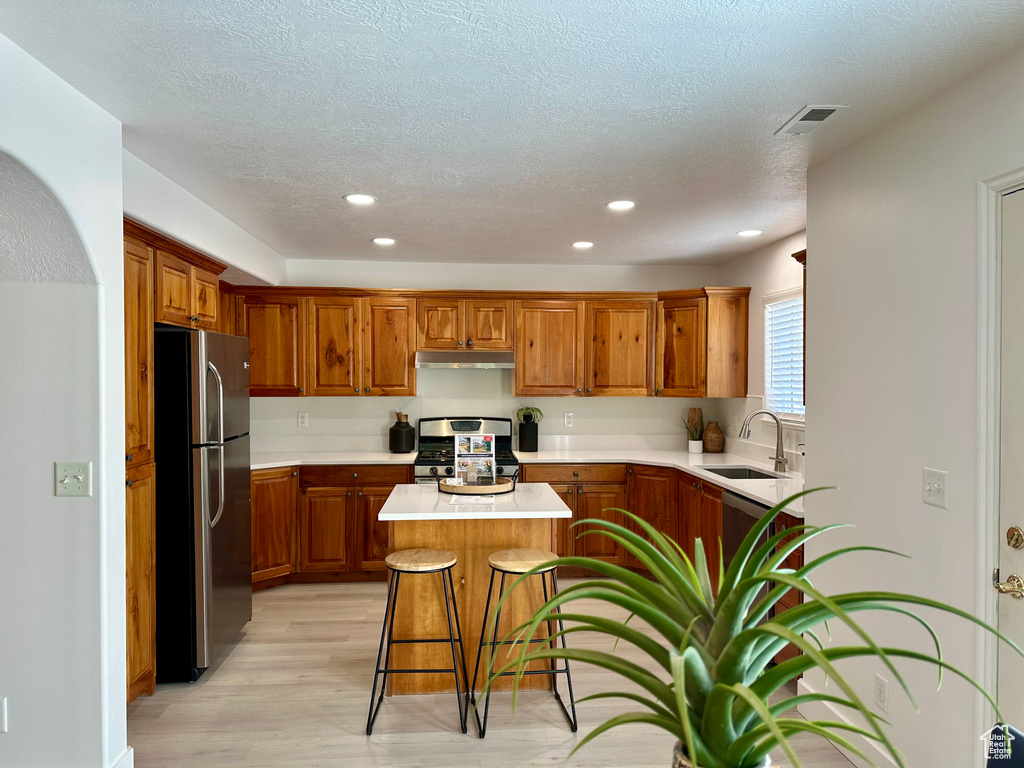 Kitchen featuring stainless steel appliances, under cabinet range hood, brown cabinets, and a sink
