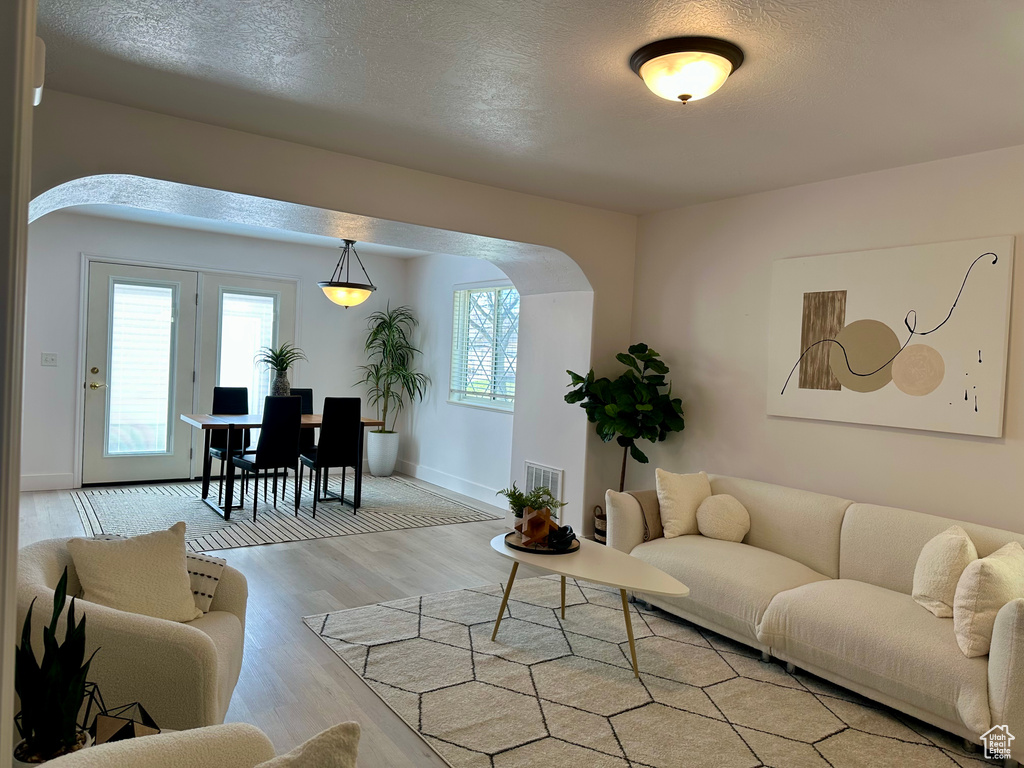 Living area featuring light wood-style floors, arched walkways, a textured ceiling, visible vents, and baseboards