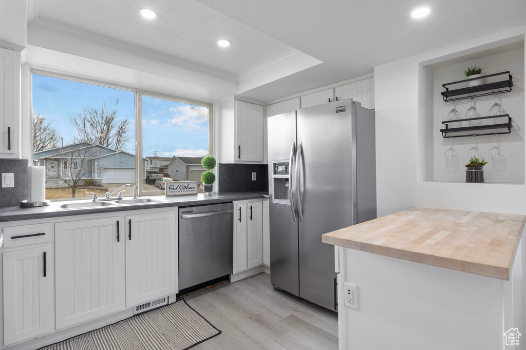 Kitchen with butcher block counters, sink, ornamental molding, stainless steel appliances, and white cabinets