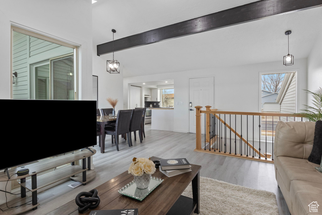 Living room featuring vaulted ceiling with beams, a notable chandelier, and light wood-type flooring