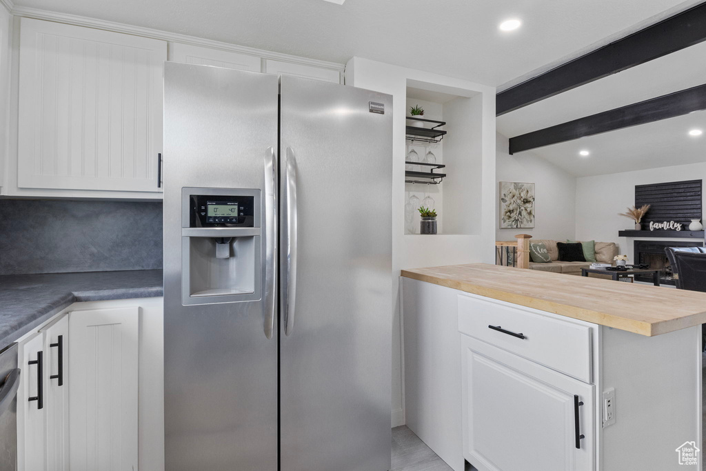 Kitchen with beamed ceiling, appliances with stainless steel finishes, wooden counters, and white cabinets