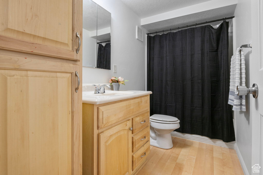 Bathroom featuring hardwood / wood-style floors, vanity, toilet, a textured ceiling, and a shower with shower curtain