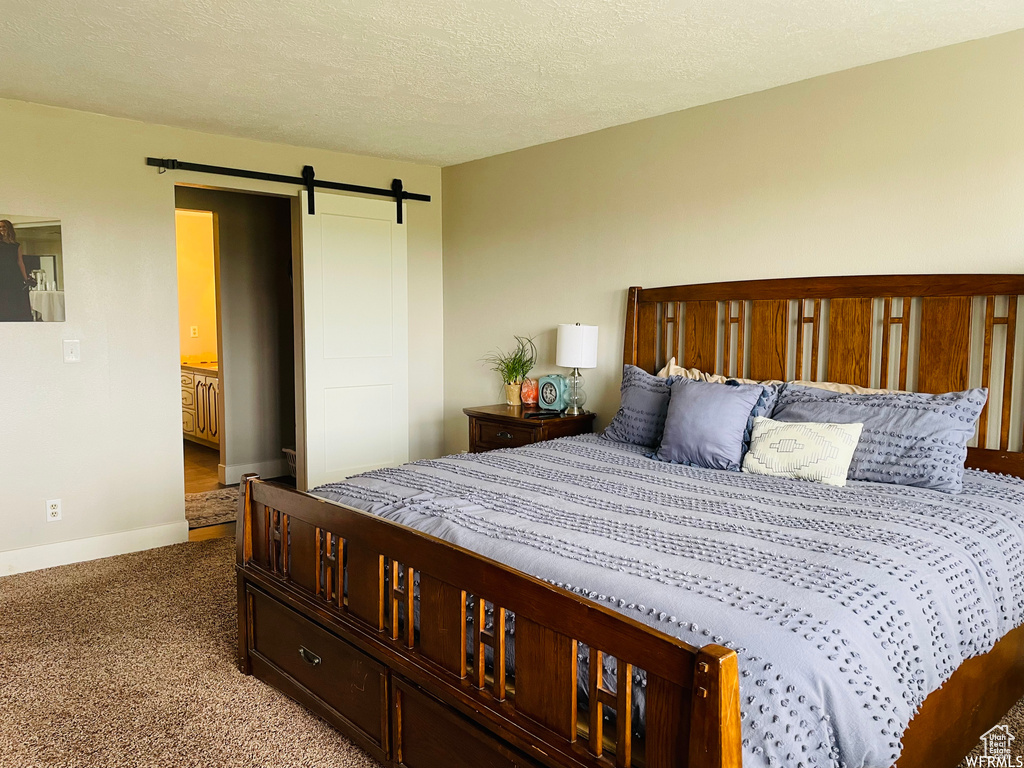 Bedroom featuring a barn door, carpet, and a textured ceiling