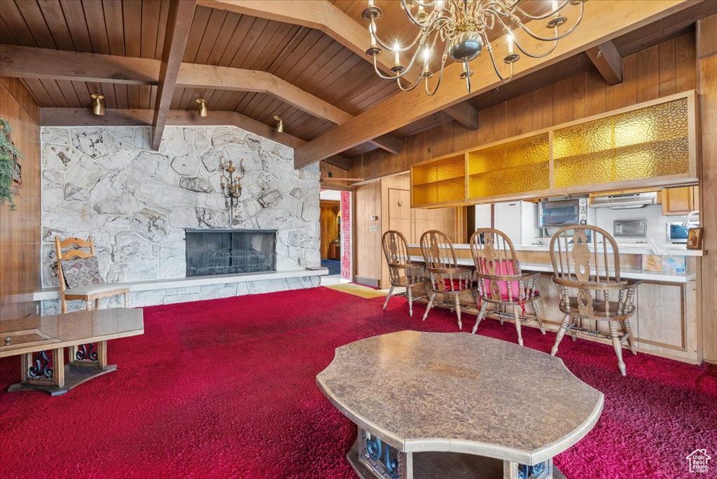 Dining room featuring a stone fireplace, an inviting chandelier, wooden ceiling, beam ceiling, and carpet