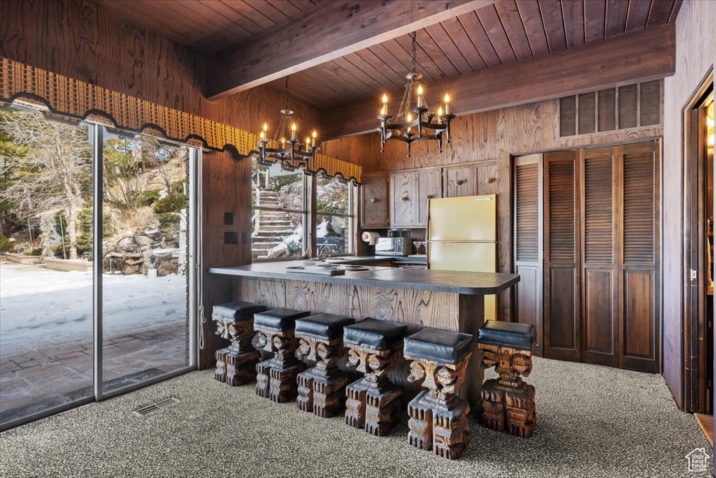 Kitchen with an inviting chandelier, wood ceiling, refrigerator, hanging light fixtures, and wooden walls