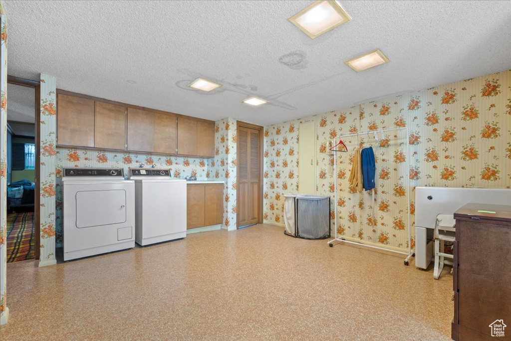 Clothes washing area with cabinets, washing machine and dryer, and a textured ceiling
