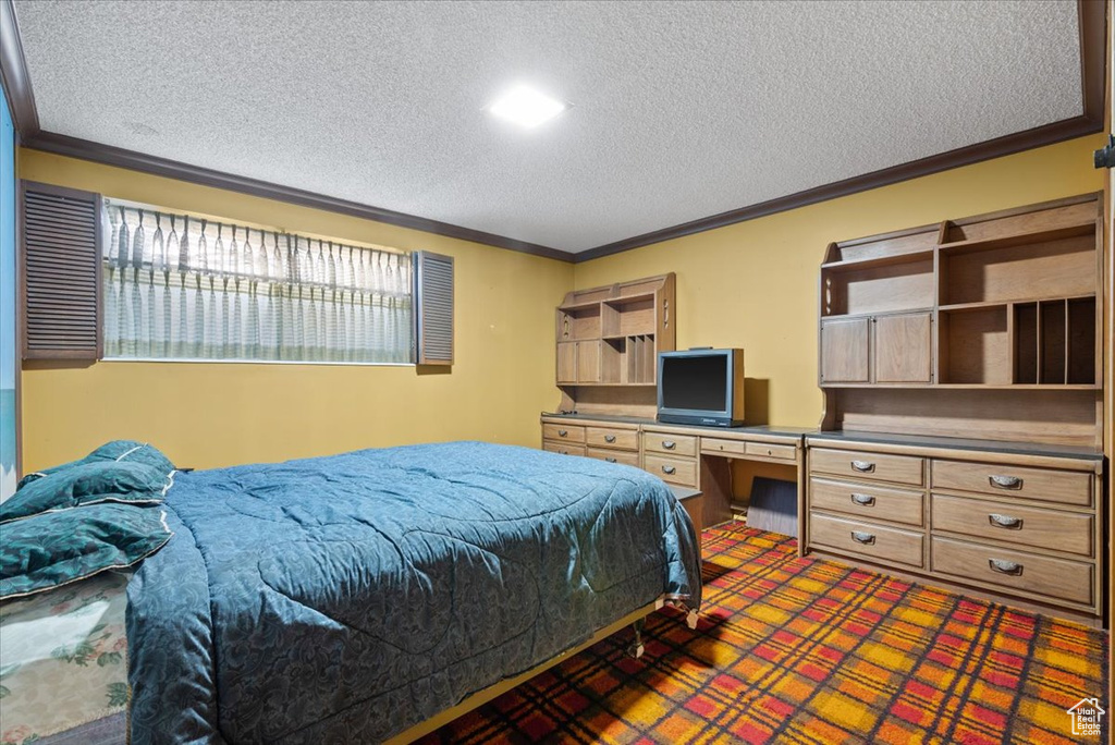 Carpeted bedroom with ornamental molding, built in desk, and a textured ceiling
