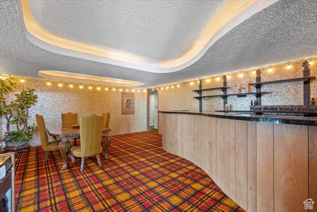 Unfurnished dining area with wooden walls, carpet floors, a tray ceiling, bar area, and a textured ceiling