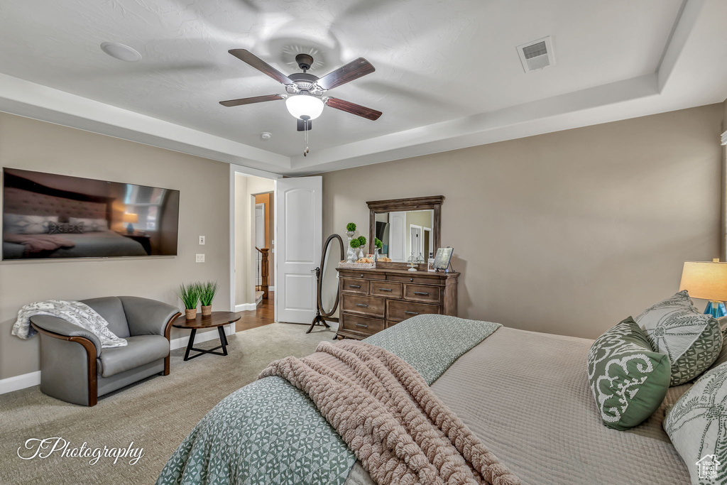 Bedroom with ceiling fan, a raised ceiling, and light carpet