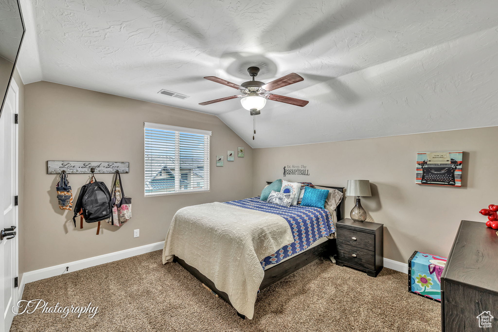 Carpeted bedroom featuring ceiling fan, lofted ceiling, and a textured ceiling