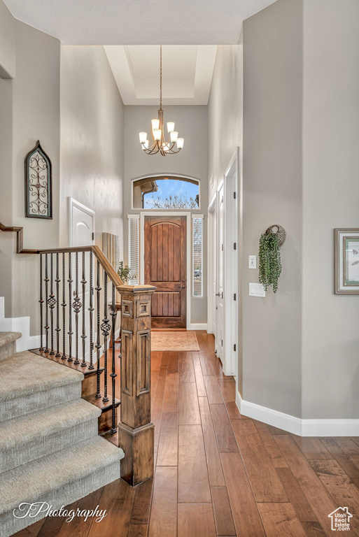 Entrance foyer with an inviting chandelier, hardwood / wood-style floors, a tray ceiling, and a high ceiling