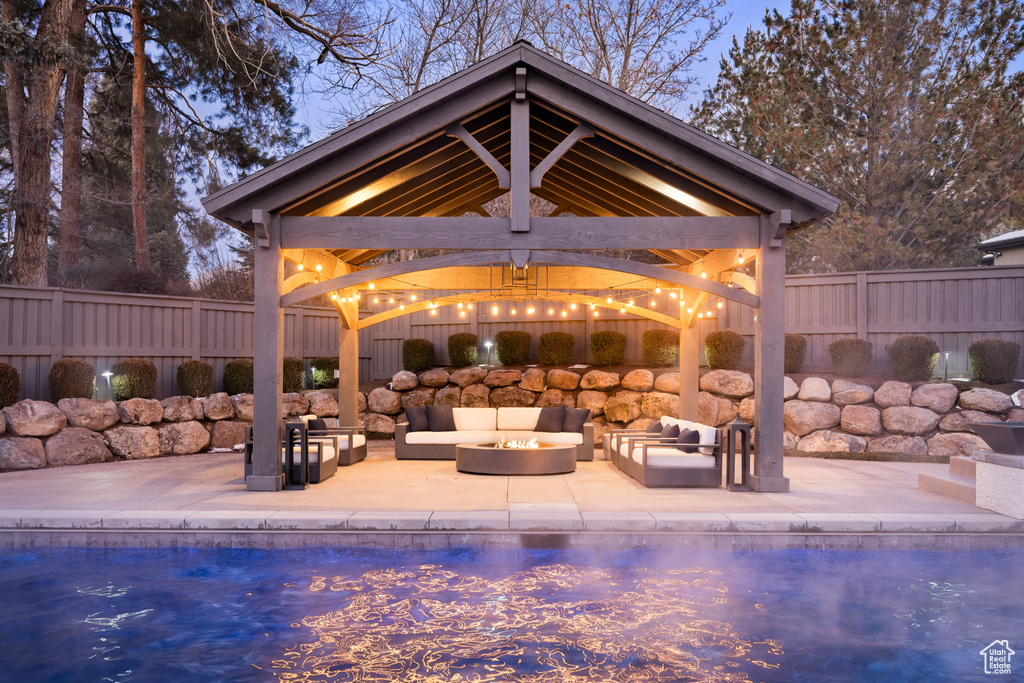 View of pool featuring a gazebo, an outdoor living space with a fire pit, a patio area, and a fenced backyard