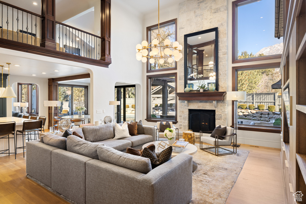 Living room featuring a stone fireplace, light wood finished floors, a towering ceiling, and a chandelier