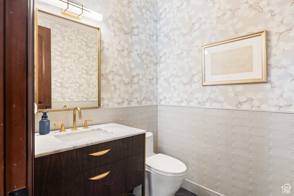 Bathroom featuring wallpapered walls, a wainscoted wall, vanity, and tile walls