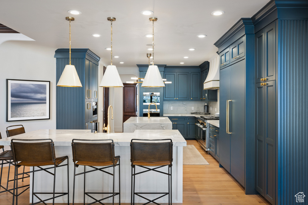 Kitchen with high quality appliances, a large island with sink, a kitchen bar, tasteful backsplash, and light stone counters