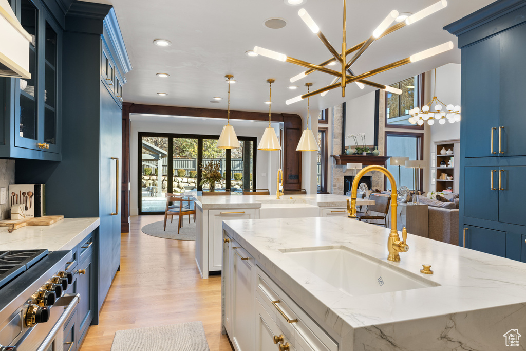 Kitchen with a kitchen island with sink, blue cabinets, a chandelier, exhaust hood, and recessed lighting