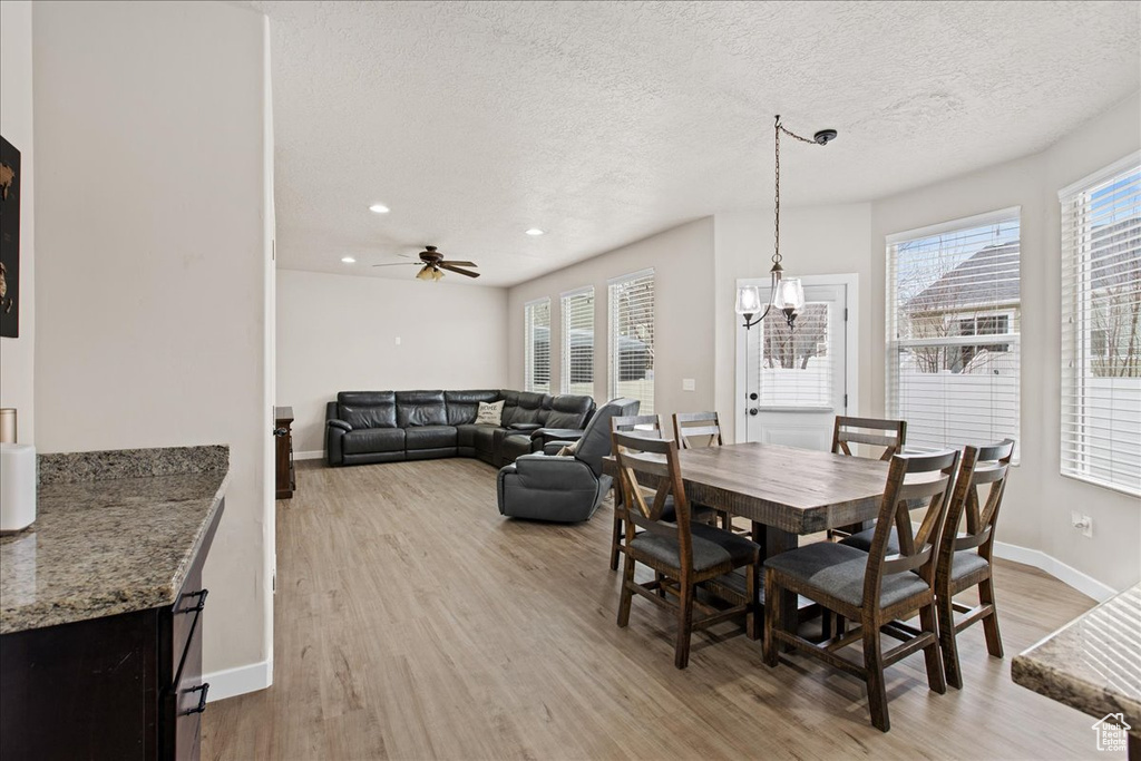 Dining space with ceiling fan with notable chandelier, light hardwood / wood-style floors, and a textured ceiling