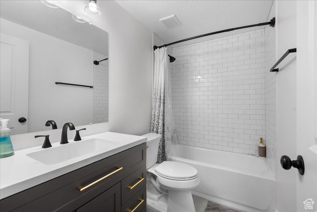 Full bathroom with vanity, shower / bath combination with curtain, a textured ceiling, and toilet