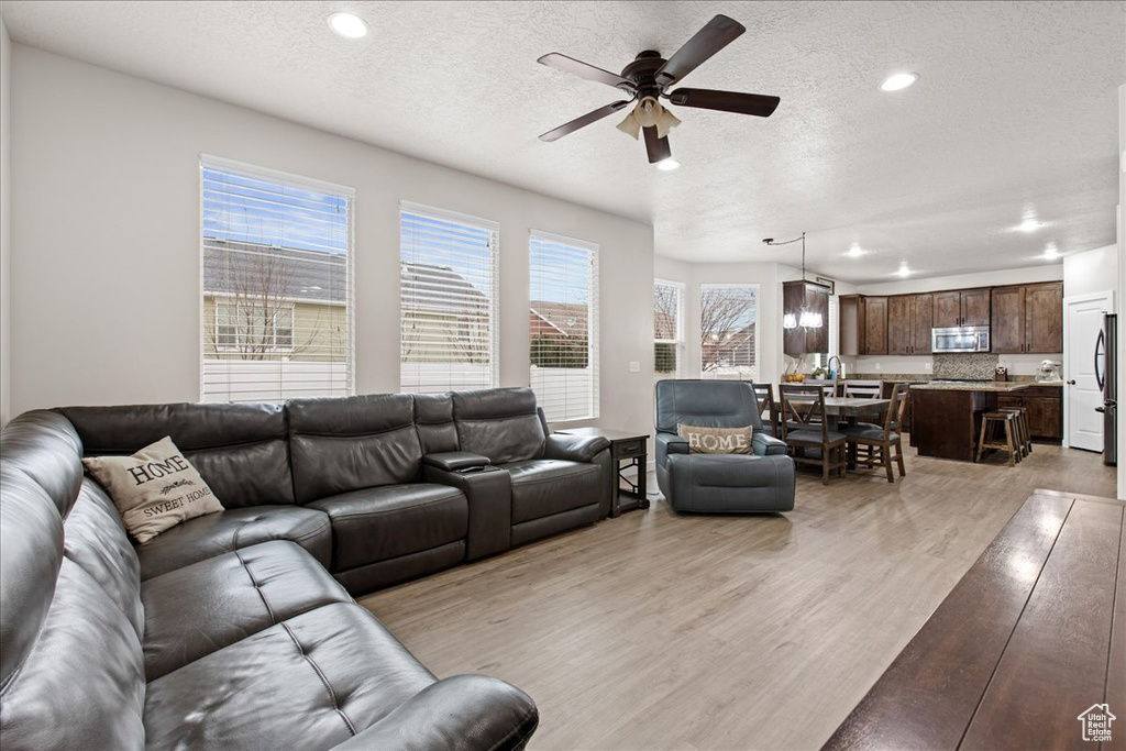 Living room with ceiling fan, a textured ceiling, and light wood-type flooring