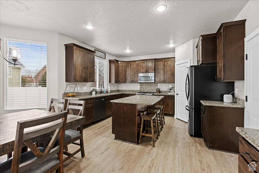 Kitchen with sink, a breakfast bar area, a center island, dark brown cabinets, and appliances with stainless steel finishes