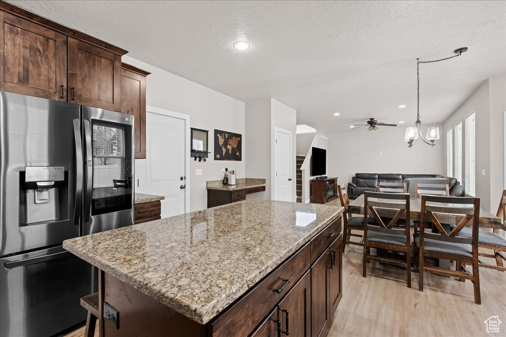 Kitchen with light wood-type flooring, stainless steel fridge, light stone countertops, and a kitchen island