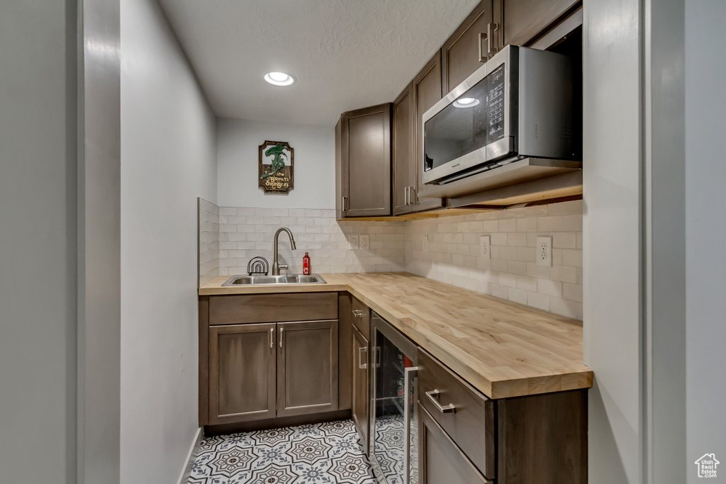 Kitchen featuring sink, wine cooler, wooden counters, backsplash, and a textured ceiling