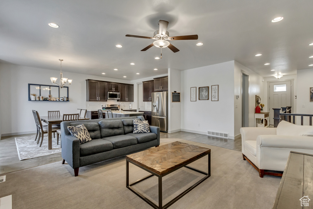 Living room featuring ceiling fan with notable chandelier and light hardwood / wood-style flooring