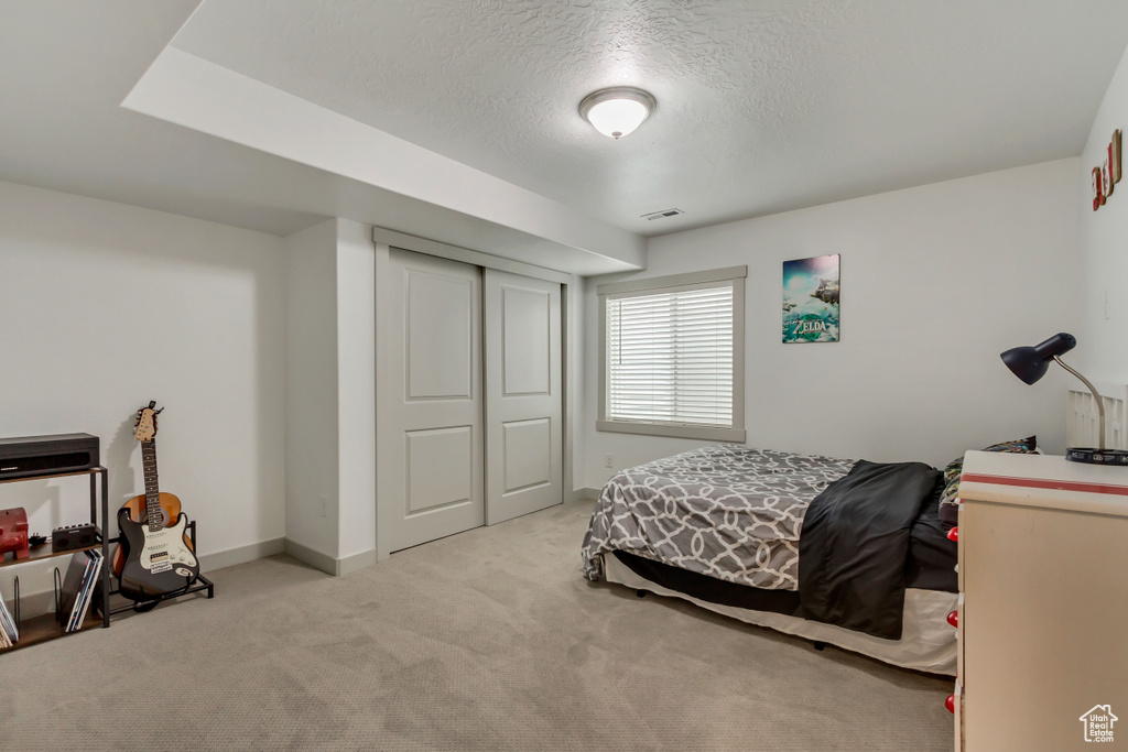Bedroom with light colored carpet, a textured ceiling, and a closet