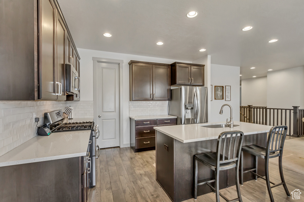 Kitchen with an island with sink, stainless steel appliances, sink, and light wood-type flooring