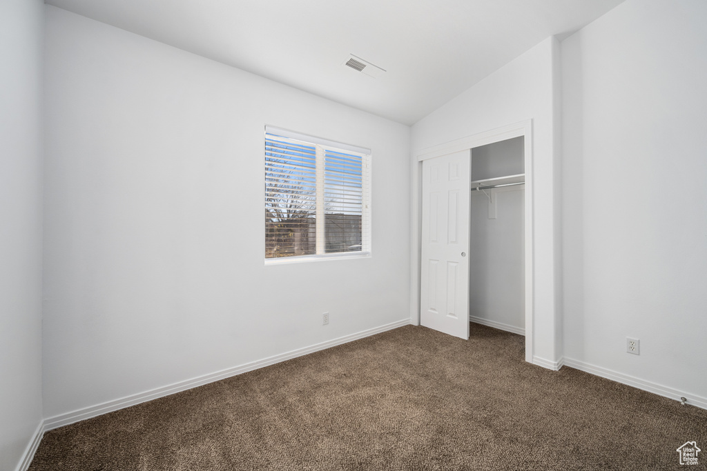 Unfurnished bedroom with lofted ceiling, dark carpet, and a closet