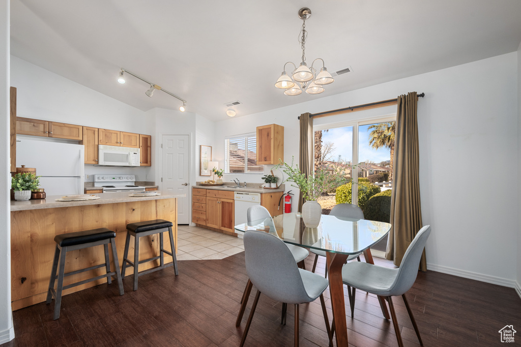 Dining area with vaulted ceiling, rail lighting, hardwood / wood-style floors, and a chandelier