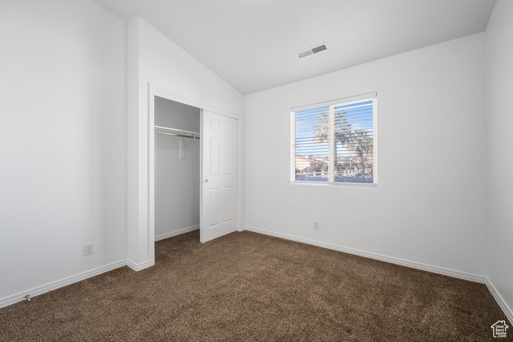 Unfurnished bedroom featuring dark carpet, vaulted ceiling, and a closet
