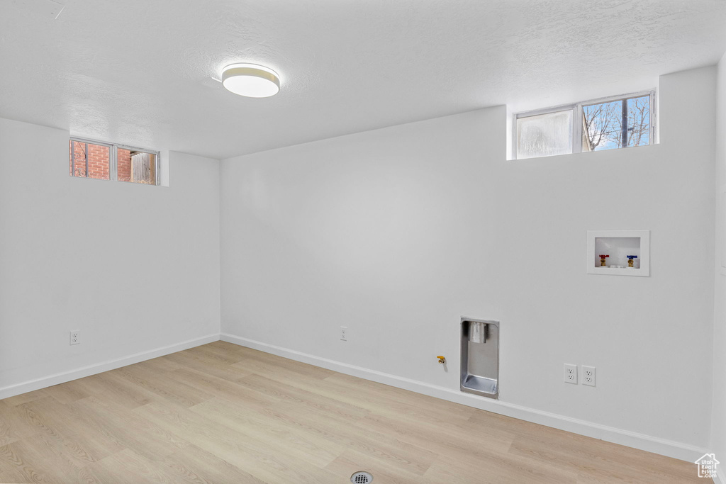 Clothes washing area with hookup for a gas dryer, washer hookup, a textured ceiling, and light wood-type flooring